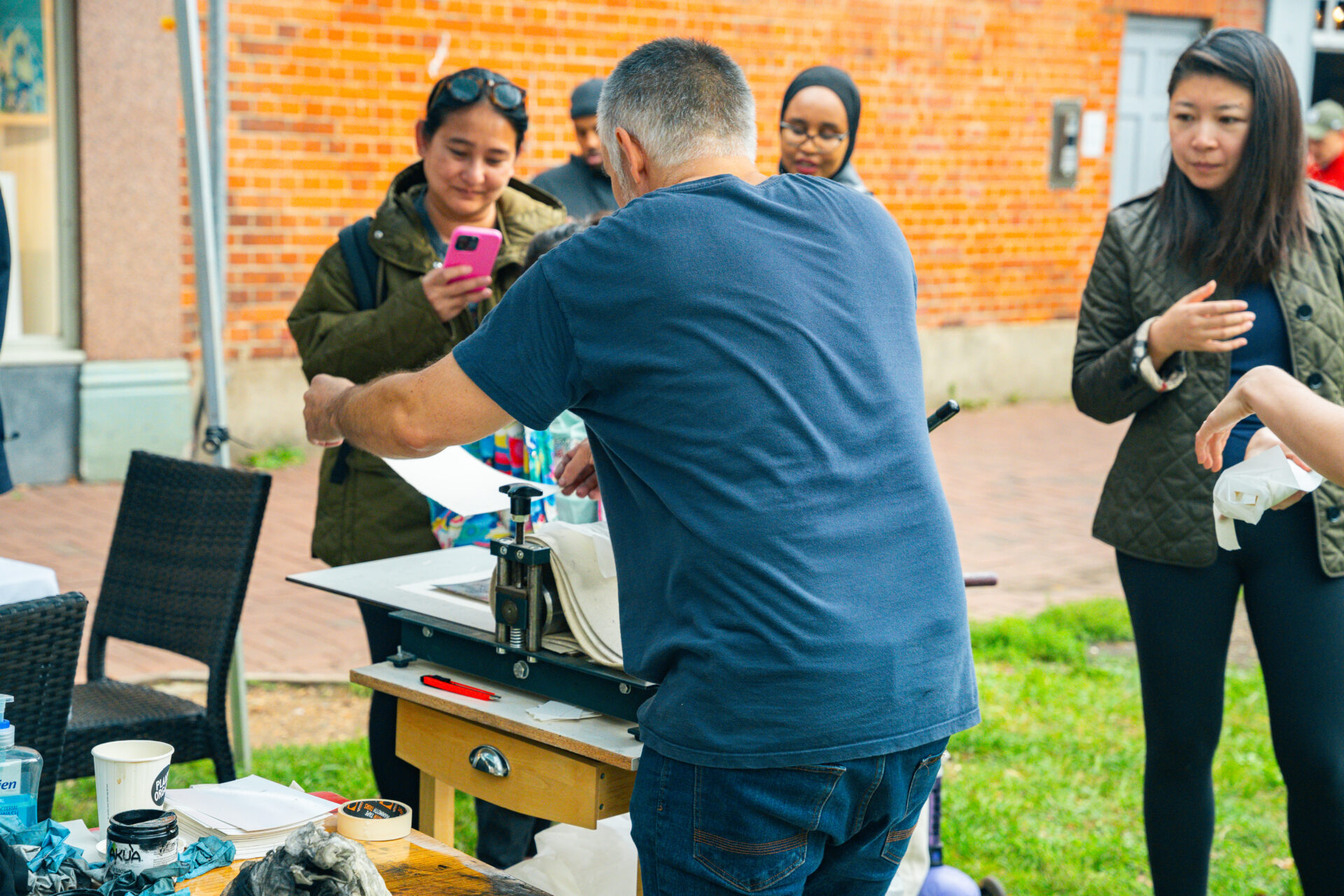 A white man shows a woman with dark hair how to print using a printing press.