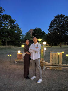 A man and a woman standing in front of an illuminated outdoor seating in park
